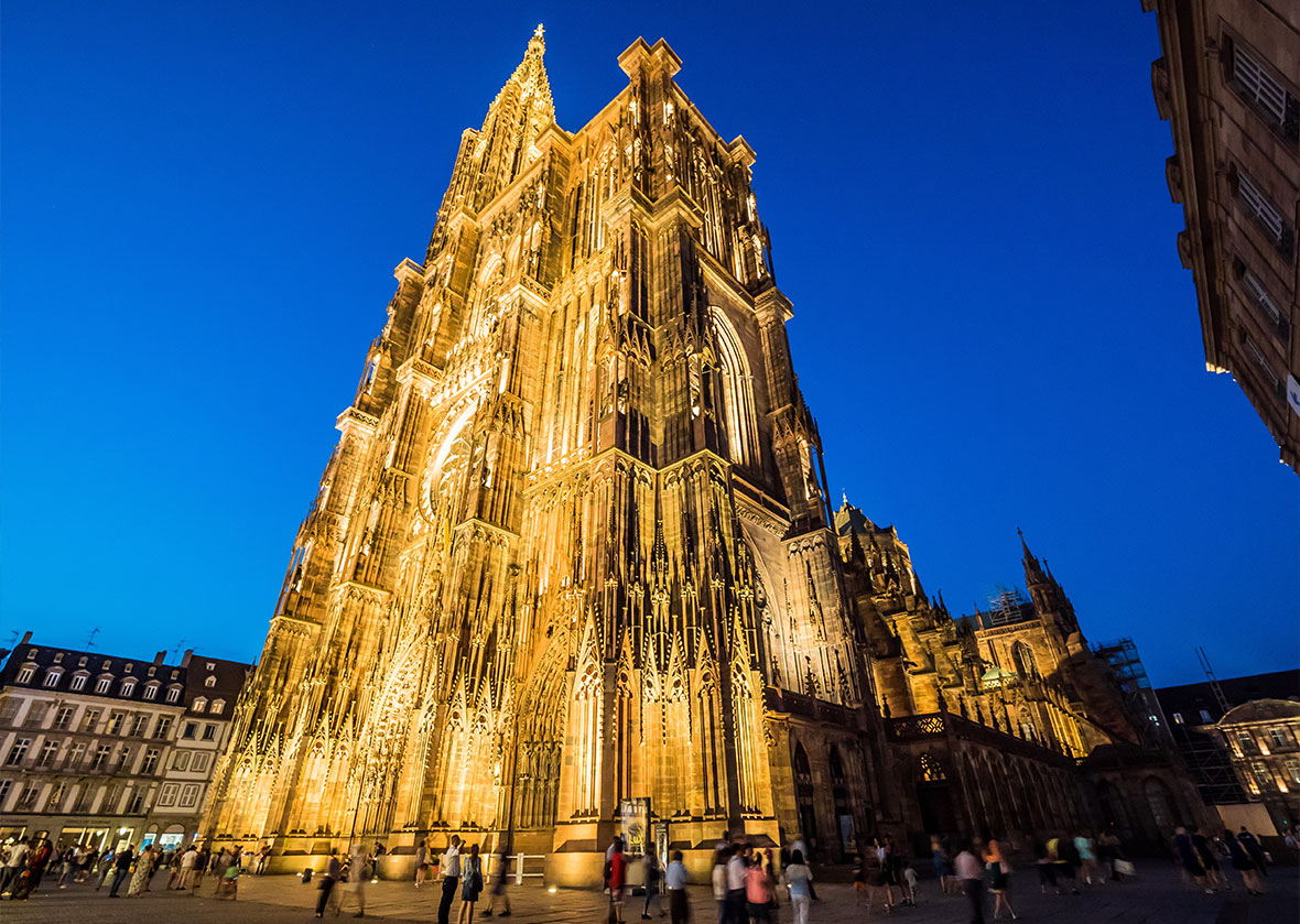 Illuminated nighttime shot of the Cathedrale Notre-Dame de Strasbourg with people around it